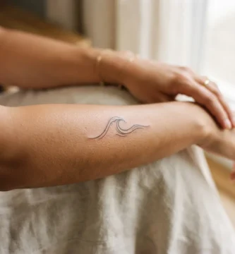 Close-up of a delicate professionally-done fine-line wave tattoo on an adult woman's inner forearm