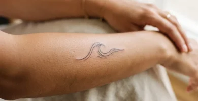 Close-up of a delicate professionally-done fine-line wave tattoo on an adult woman's inner forearm