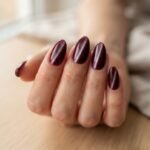 Close-up of deep burgundy velvet nails on almond-shaped nails showing the plush shifting shimmer effect