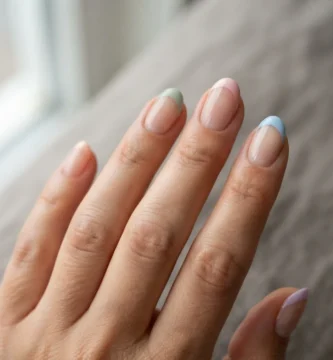 Close-up of five nails with colored french tips in soft pastel shades including lavender, sage green, and blush pink on a natural light-medium skin tone hand against a clean white background.