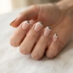 Close-up of finished chrome double french nails on a realistic hand showing two parallel curved tip lines with a mirror-finish chrome outer arch and a thin white inner line against a soft nude base.