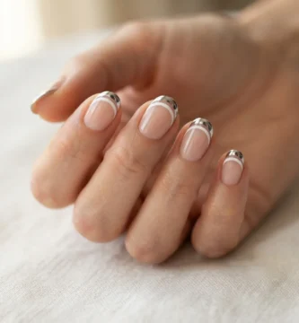 Close-up of finished chrome double french nails on a realistic hand showing two parallel curved tip lines with a mirror-finish chrome outer arch and a thin white inner line against a soft nude base.