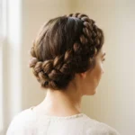 Finished dutch braid crown halo style on a woman with medium brown hair, soft natural window lighting, close-up on the raised braid texture wrapping the head.