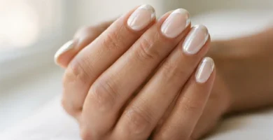Close-up of a chrome glazed-donut French tip manicure on medium-toned hands with a mirror-finish white pearl tip and sheer nude base, photographed in soft natural window light.