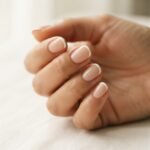 Close-up of a micro french manicure on short natural nails with a sheer nude base and a thin precise white tip line in soft natural window light.