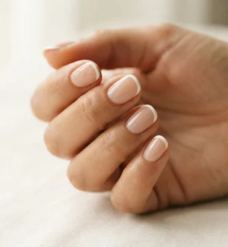 Close-up of a micro french manicure on short natural nails with a sheer nude base and a thin precise white tip line in soft natural window light.