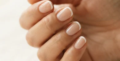 Close-up of a micro french manicure on short natural nails with a sheer nude base and a thin precise white tip line in soft natural window light.