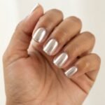 Close-up of short square nails with a glossy glazed donut chrome finish on a warm-toned hand against soft natural light.