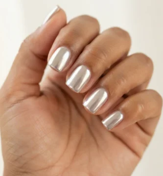 Close-up of short square nails with a glossy glazed donut chrome finish on a warm-toned hand against soft natural light.